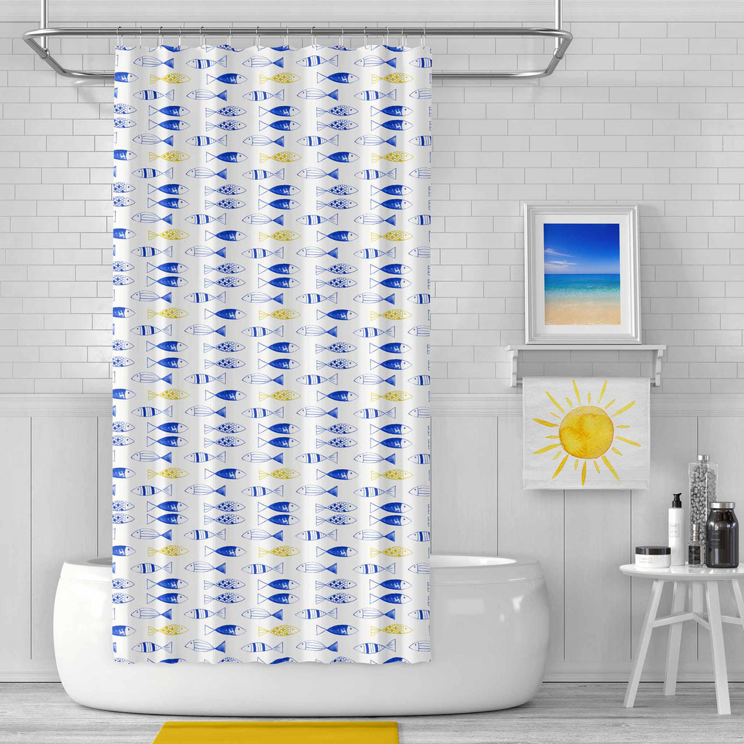 Bright and modern bathroom featuring a shower curtain with a playful blue and yellow fish pattern. The room includes a white subway tile backdrop, a framed beach photograph, a yellow sun towel, and minimalist decor, creating a fresh and coastal-inspired atmosphere.