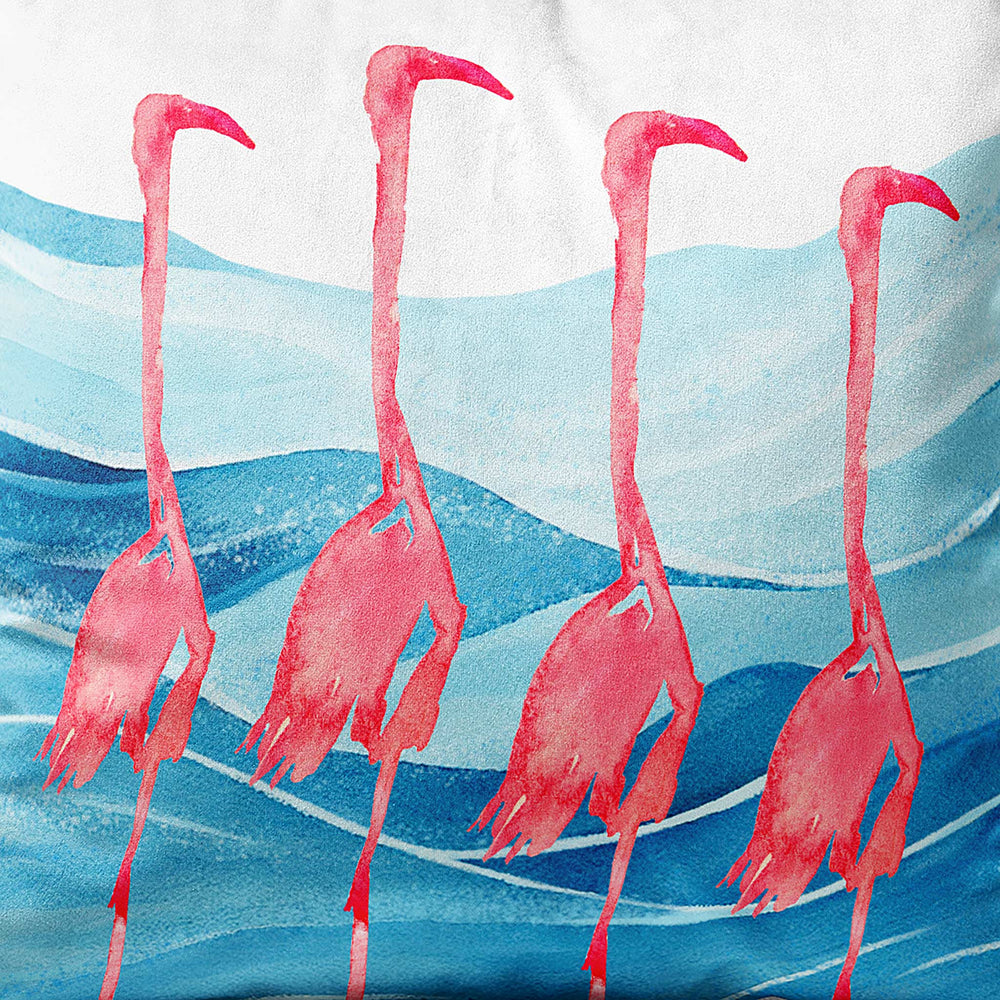 Close-up view of a square throw pillow featuring four watercolor flamingos standing in blue ocean waves, creating a coastal-inspired home decor accent.
