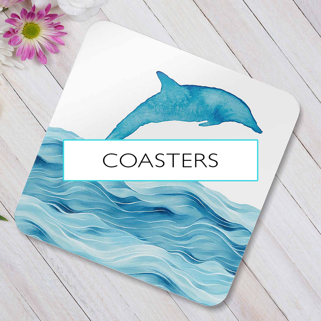 A set of ocean-themed coasters featuring a dolphin design and watercolor waves, placed on a white wooden surface with a pink flower nearby. A transparent overlay with the word “COASTERS” highlights the collection.