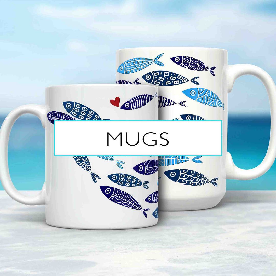 Two white ceramic mugs with a blue and white fish pattern, featuring one fish with a small red heart. The mugs are set against a tropical ocean backdrop on a light surface. A label reading “MUGS” overlays the image, highlighting the collection.