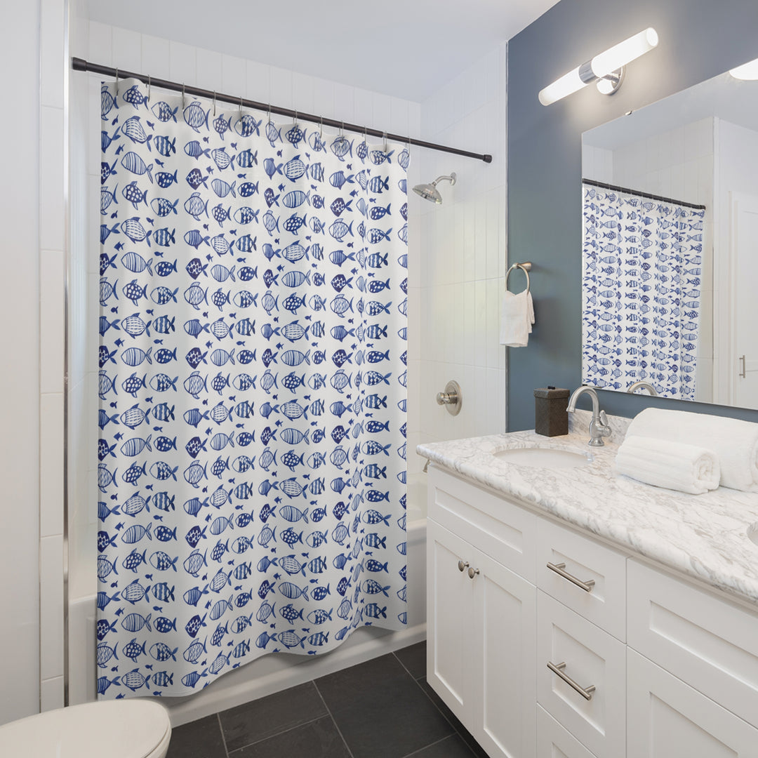 Blue and white fish-pattern shower curtain installed in a contemporary bathroom with a marble countertop, white cabinetry, and a navy accent wall.
