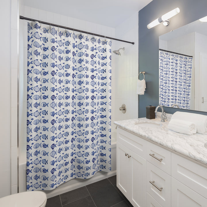 Blue and white fish-pattern shower curtain installed in a contemporary bathroom with a marble countertop, white cabinetry, and a navy accent wall.