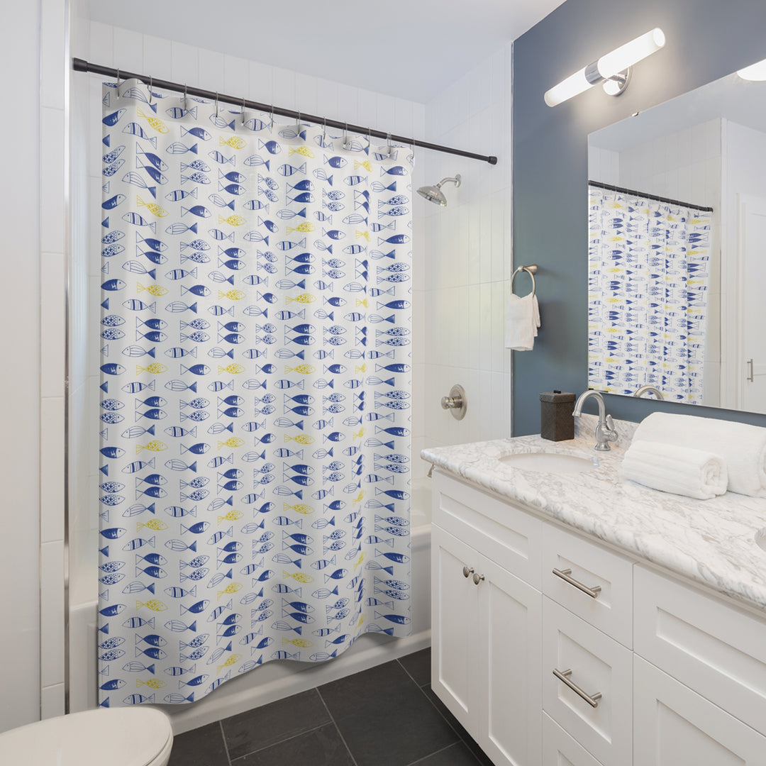 Modern bathroom featuring a bright and playful shower curtain with a repeating blue and yellow fish pattern. The white vanity with a marble countertop, dark tile floor, and navy accent wall complement the decor, creating a clean and inviting space.