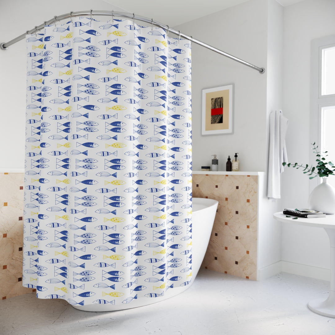 Modern bathroom featuring a freestanding bathtub and a shower curtain with a whimsical blue and yellow fish pattern on a white background. The space includes a small side table with a vase and books, a wall-mounted towel, and minimalist decor for a fresh and serene atmosphere.