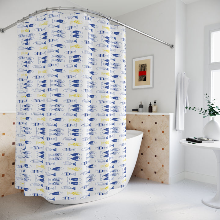 Modern bathroom featuring a freestanding bathtub and a shower curtain with a whimsical blue and yellow fish pattern on a white background. The space includes a small side table with a vase and books, a wall-mounted towel, and minimalist decor for a fresh and serene atmosphere.
