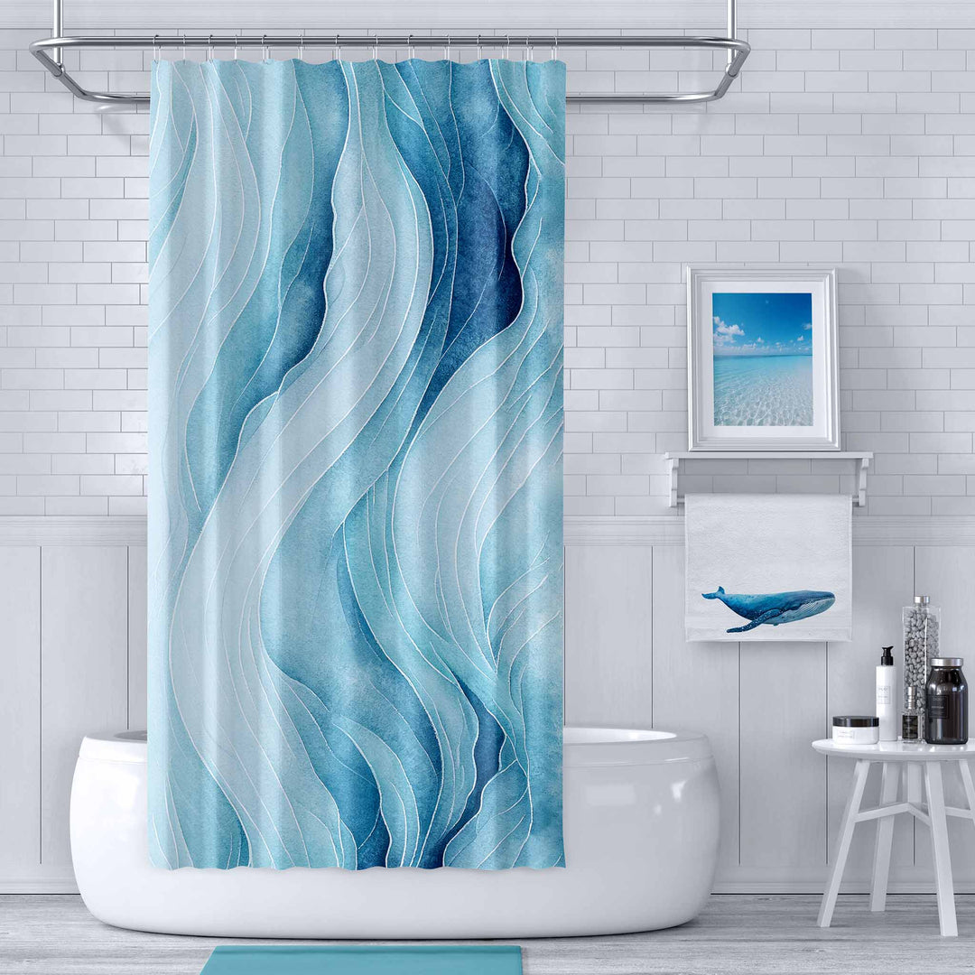 Abstract wave-pattern shower curtain in shades of blue hanging in a serene coastal-inspired bathroom. The space features a white subway tile backdrop, a framed ocean photograph, and a towel with a whale design, creating a calming and modern aesthetic.