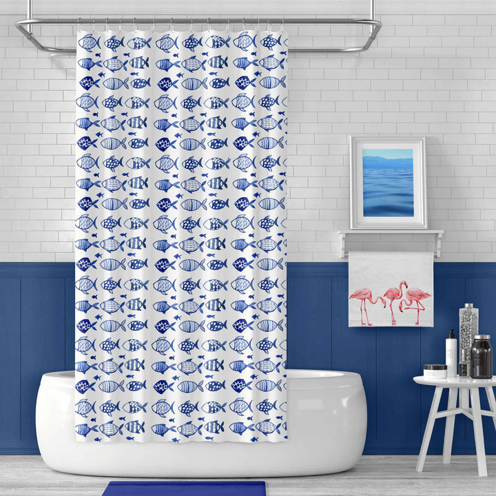 Blue and white fish-pattern shower curtain hanging in a modern coastal bathroom with navy accents, a freestanding tub, and minimalist decor.