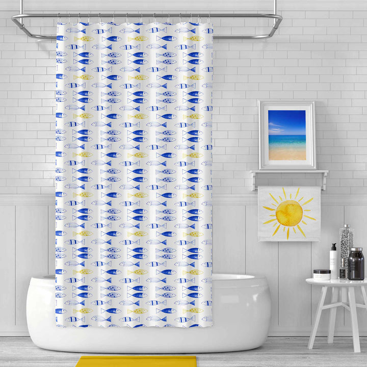 Bright and modern bathroom featuring a shower curtain with a playful blue and yellow fish pattern. The room includes a white subway tile backdrop, a framed beach photograph, a yellow sun towel, and minimalist decor, creating a fresh and coastal-inspired atmosphere.