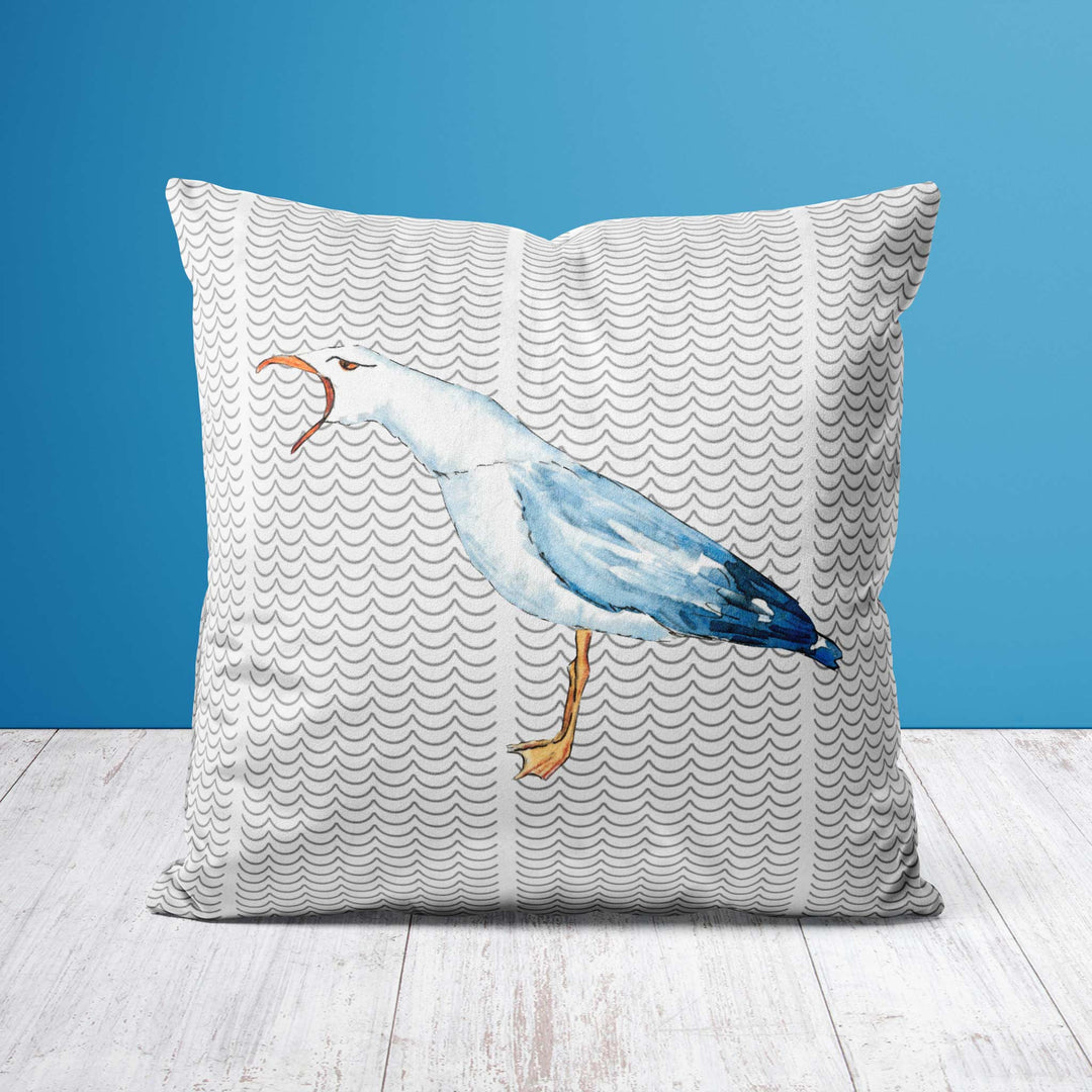 Square throw pillow featuring a watercolor-style illustration of a light blue seagull squawking against a white background with a repeating wave pattern. The pillow is set against a blue backdrop with a wooden floor, enhancing its coastal and nautical theme.