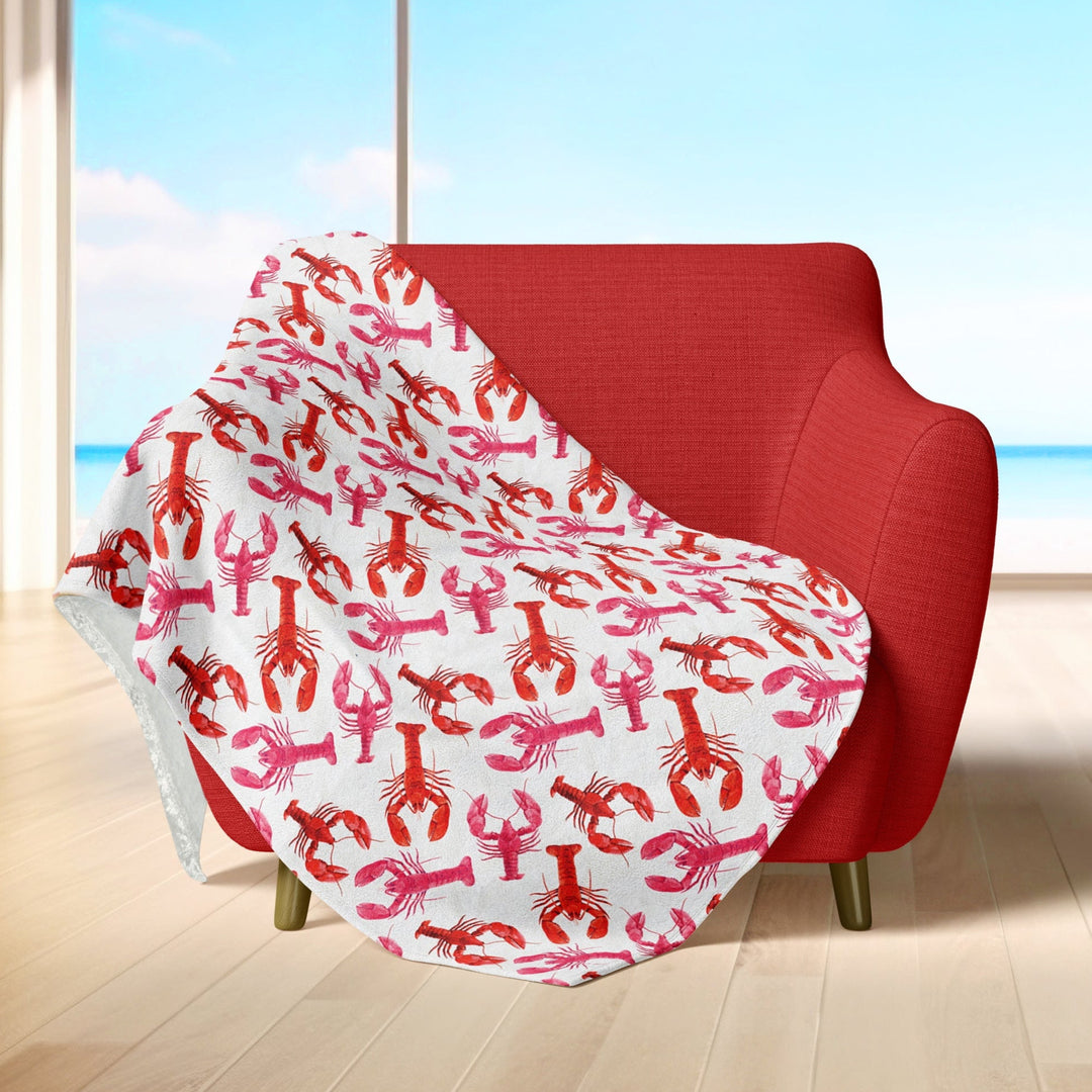 Cozy red and pink lobster-patterned throw blanket draped over a red armchair in a bright room with large windows showcasing a beautiful ocean view.